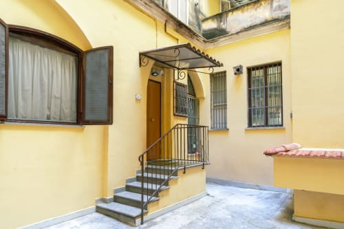 Luminoso ingresso giallo della Casa Verde di Astrachan a Roma con scale in metallo, porta in legno, finestre con inferriate