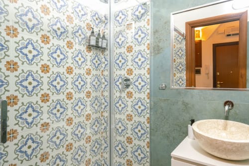 Bagno moderno nello studio di Roma con doccia con piastrelle blu e arancioni decorative, lavabo in pietra rotondo e specchio