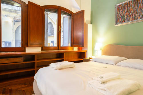 Elegante monolocale a Roma con scrivania in legno, letto matrimoniale, parete verde e finestre con vista sulla città