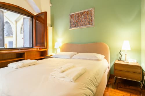 Camera da letto luminosa a Roma con letto in legno, pareti verdi, pavimento in legno, scrivania e vista sulla città
