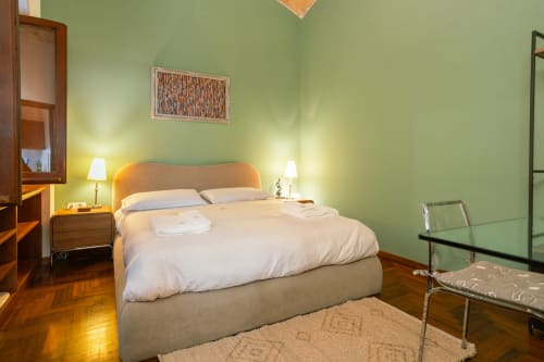 Elegante camera da letto in monolocale a Roma con pareti verde salvia, letto matrimoniale, comodini in legno, illuminazione soft e parquet