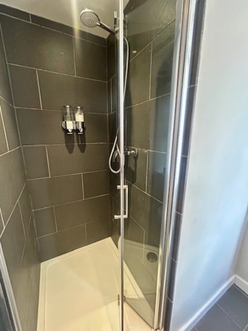 Modern walk-in shower with dark tiled walls, rainfall showerhead, and glass enclosure in Superior King Room at The Railway