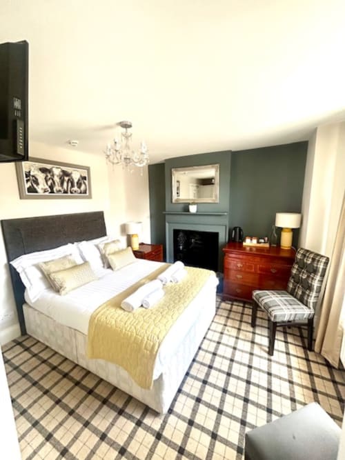 Cookson Deluxe Double Room at The Railway Hotel Haydon Bridge, featuring a bed with yellow throw, fireplace with mirror, red