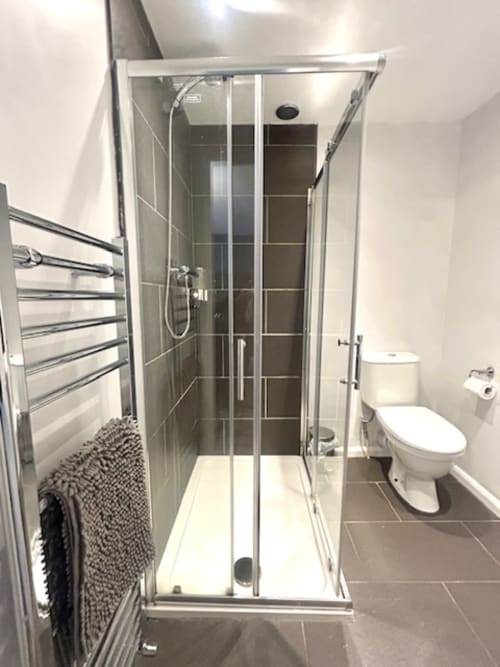 Modern bathroom in Railway Hotel Haydon Bridge with walk-in shower, toilet, heated towel rack, and dark tile flooring