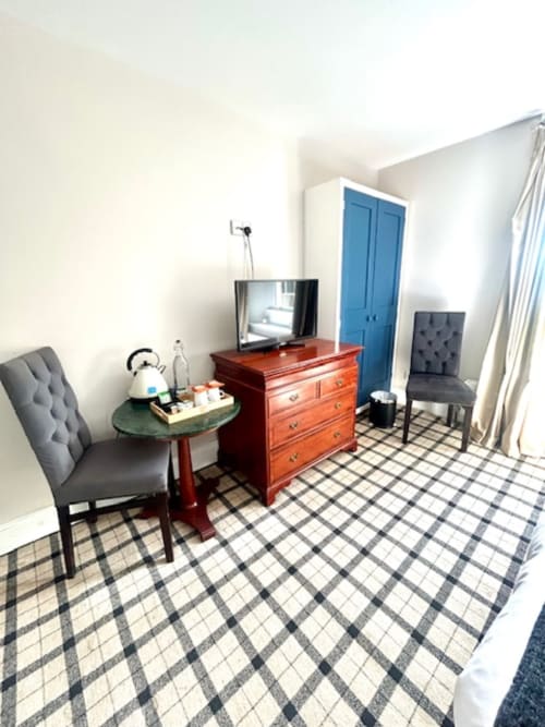 Superior King Room at The Railway Hotel with wooden dresser, TV, grey upholstered chairs, blue wardrobe, and checkered floor