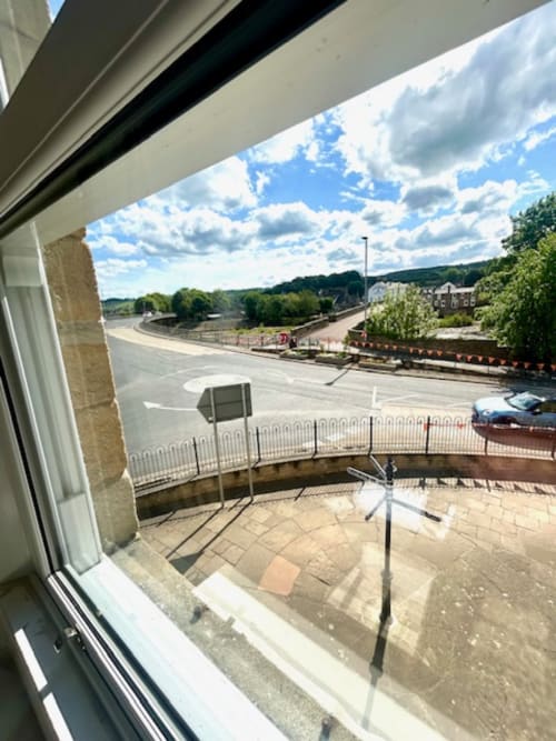 View from Ratcliffe room at The Railway Hotel showing Haydon Bridge river, parking area, and surrounding woodland under blue