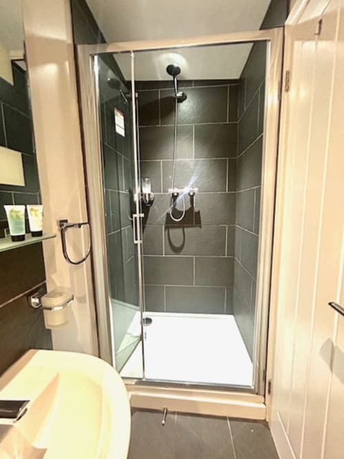 Modern bathroom at The Railway Hotel Haydon Bridge with walk-in shower, dark tile walls, and cream fixtures