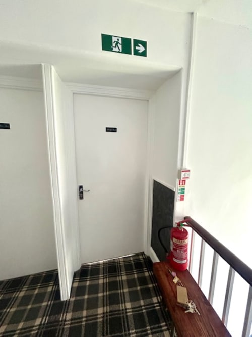 Emergency exit corridor with green exit sign, red fire extinguisher, and white doors at The Railway Hotel Haydon Bridge