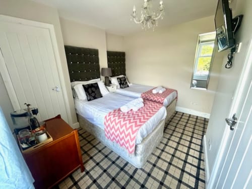 Twin beds with dark headboards in Shaftoe room at The Railway Hotel Haydon Bridge, featuring checkered floor and flat-screen