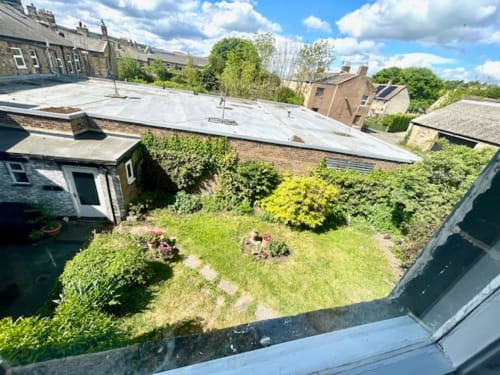 Overgrown garden courtyard at The Railway Hotel Haydon Bridge with stone buildings, wild vegetation, and flat roof structures