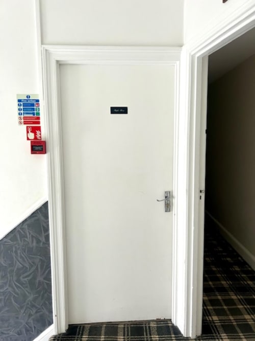 White corridor door at Railway Hotel Haydon Bridge with safety signage and fire equipment visible on left wall