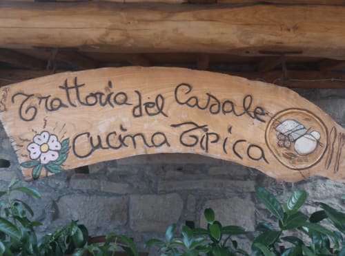 Insegna in legno intagliato della Trattoria del Caddale Cucina Tipica a Floresta, Italia, con fiori decorativi e stile tradizionale