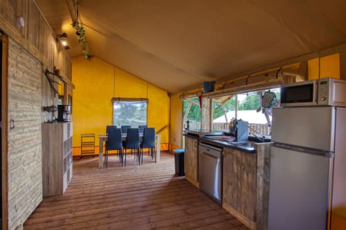 Helder geel glamping tentinterieur met keuken, eetgedeelte en houten meubels bij Home Sweet Lodge Aquitaine