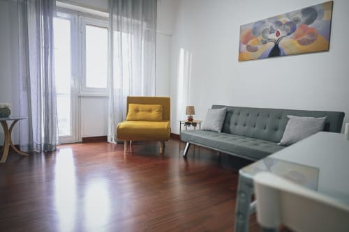 Soggiorno moderno a Roma con poltrona gialla, divano verde, pavimenti in legno e vista sulla città dal balcone