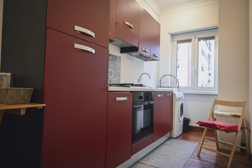 Moderna cucina rossa in appartamento romano con fornello, lavatrice e vista sulla città dalle finestre