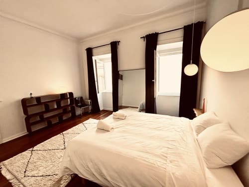 Modern bedroom in Royal Prince Garden Apartments, Lisbon, featuring extra-long bed, dark curtains, wooden shelving, and