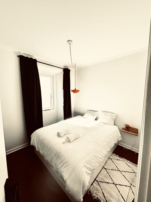 Modern bedroom at Royal Prince Garden Apartments in Lisbon with white bed, black curtains, and pendant light