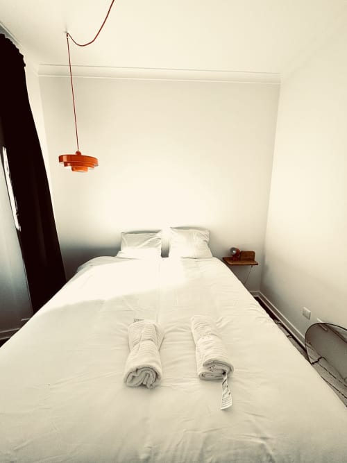 Minimalist bedroom with white bed, rolled towels, orange pendant lamp at Royal Prince Garden Apartments, Lisbon