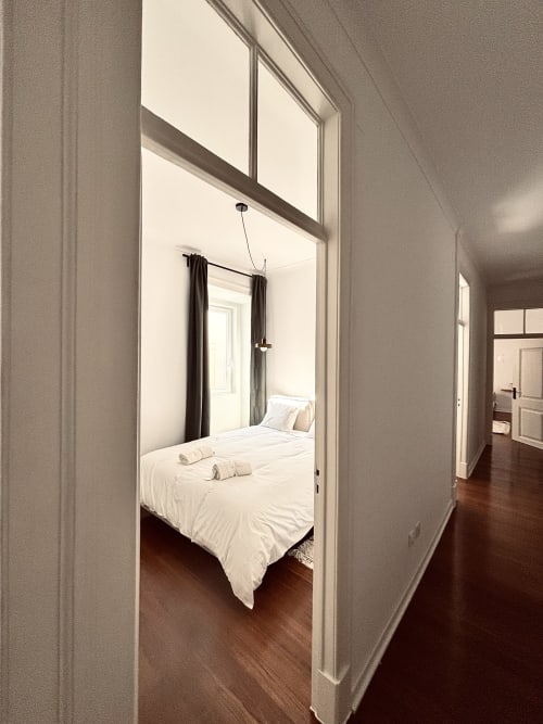 Modern bedroom hallway in Royal Prince Garden Apartments Lisboa, featuring white bedding and dark wood flooring with garden