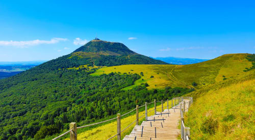 Scenic hiking trail overlooking Puy de Dôme volcano and lush green landscape near Riom, France