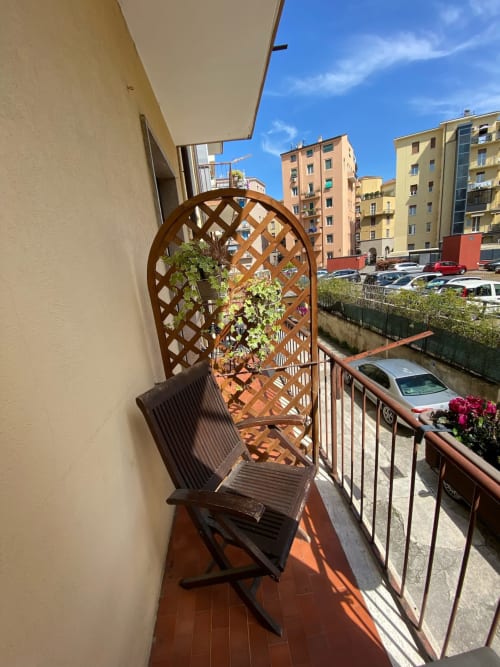Balcone soleggiato dell'hotel Le Arche a Verona con pergolato in legno, sedia, piante fiorite e vista sulla città