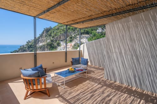 Terrazza soleggiata di La Conciergerie Capri con sedie in legno, cuscini blu e vedute panoramiche della costa caprese