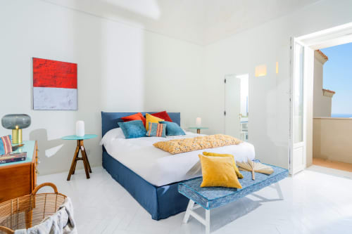 Camera luminosa a La Conciergerie Capri con letto blu, cuscini colorati e balcone con vista mare