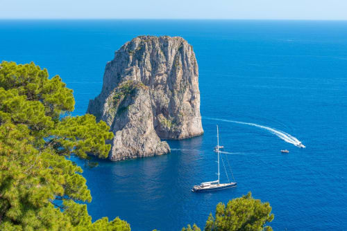 Barca a vela ancorata presso la drammatica formazione rocciosa calcarea al largo della costa di Capri con il turchese Mar Mediterraneo