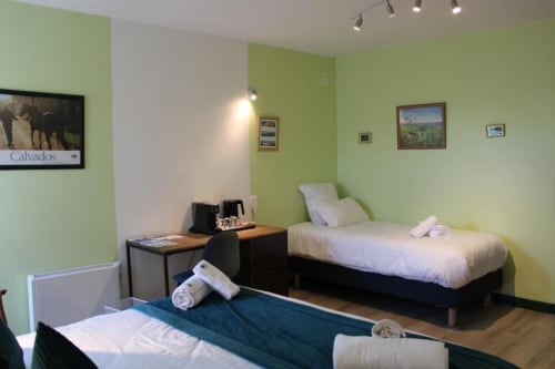 Triple bedroom at Domaine des Piéris with two beds, green walls, and garden view in Grandcamp-Maisy