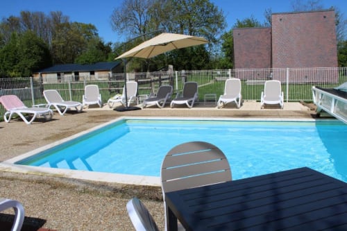 Outdoor swimming pool with lounge chairs and umbrella at Domaine des Piéris in Grandcamp-Maisy