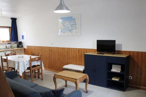Cozy cottage living room at Domaine des Piéris with wooden wainscoting, dining table, TV, and garden views in Normandy