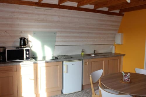 Bright kitchen area in Domaine des Piéris cottage with wooden cabinets, microwave, refrigerator, and dining table in