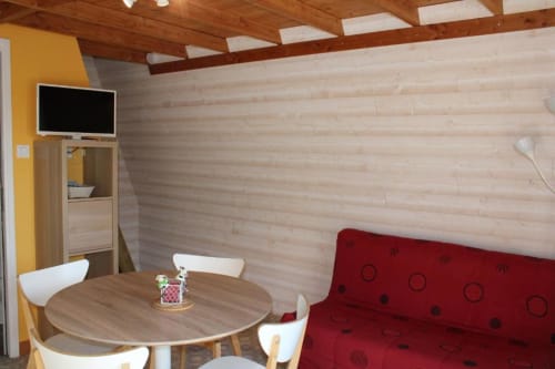 Cozy wooden cottage interior with red sofa, dining table, TV, and yellow accent wall at Domaine des Piéris, Grandcamp-Maisy