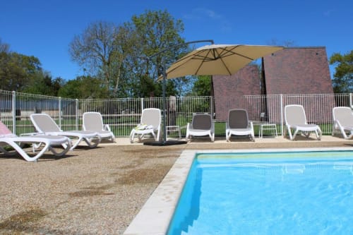 Pool deck at Domaine des Piéris with lounge chairs, umbrella, and trees in Grandcamp-Maisy