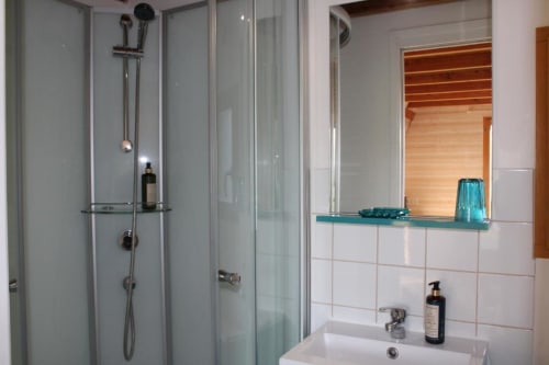 Modern bathroom with glass shower enclosure, white sink, and turquoise glass shelf at Domaine des Piéris cottage in