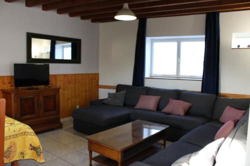 Spacious living room with black sectional sofa, wooden furniture, TV, and garden views at Domaine des Piéris cottage in