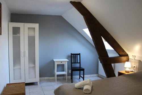 Attic bedroom at Domaine des Piéris cottage in Grandcamp-Maisy with exposed beams, bed, white wardrobe, and garden view