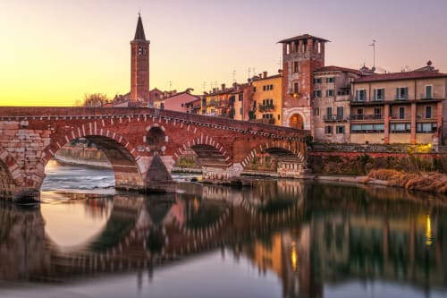 Ponte Pietra che attraversa il fiume Adige al tramonto a Verona, con edifici storici e campanile riflessi nell'acqua