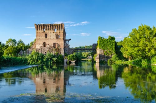 Rovine di un'antica torre in pietra riflessa nel fiume vicino a Verona, Italia