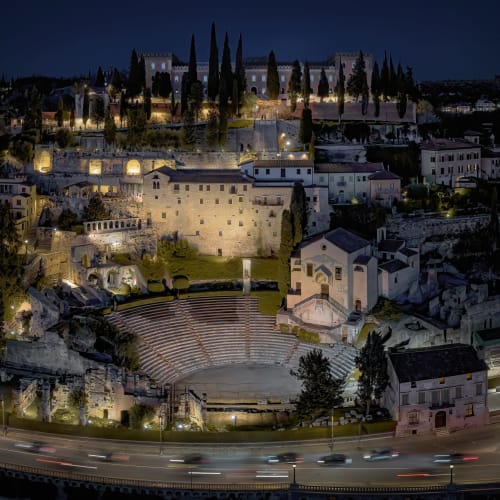 L'anfiteatro romano illuminato di Verona di notte con fortezza medievale e cipressi nel paesaggio storico della città