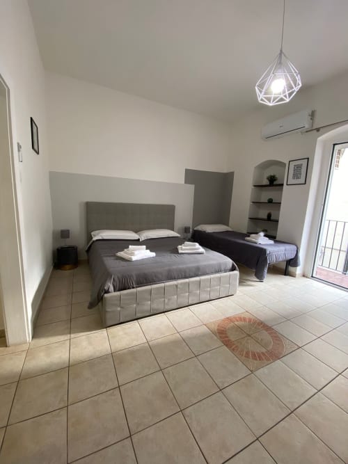 Modern bedroom at Newhouse hotel in Bari with twin beds, tiled flooring, geometric pendant light, and balcony access