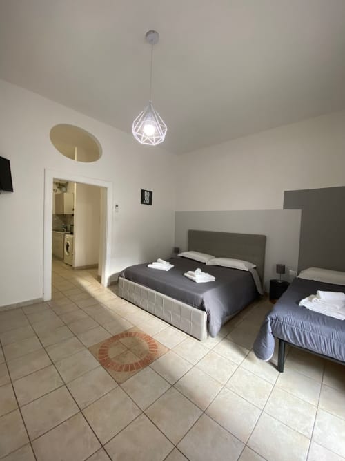 Camera moderna con due letti, lampada sospesa bianca, pavimento piastrellato e accesso al bagno presso Newhouse Bari