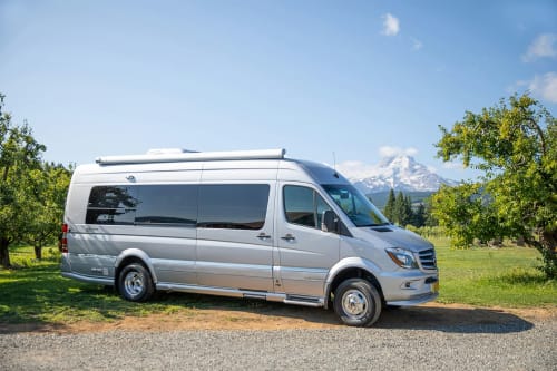 Silver campervan parked in rural setting with snow-capped mountain backdrop near Torre Boldone, Bergamo