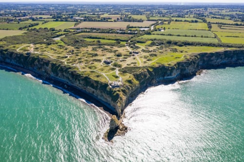 Aerial view of Domaine des Piéris cliffside B&B in Grandcamp-Maisy with turquoise waters and green farmland