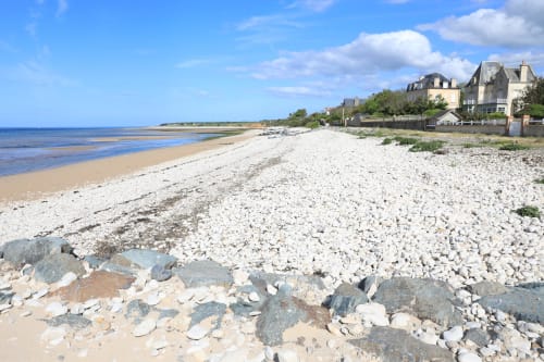 Pebble beach at Domaine des Piéris in Grandcamp-Maisy with historic stone houses overlooking the Normandy coastline under