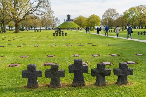Stone crosses in military cemetery near Grandcamp-Maisy, Normandy with visitors and memorial monument