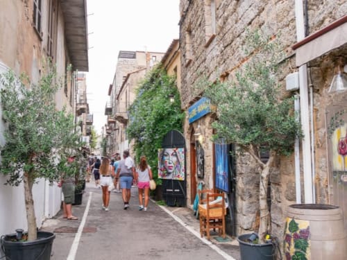 Affascinante strada stretta a Lecci con edifici in pietra ricoperti di edera, negozi e turisti che camminano per il vicolo del villaggio