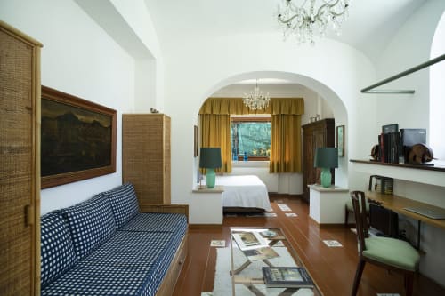 Elegante suite a La Conciergerie Capri con divano blu, arco, tende dorate e vista piscina