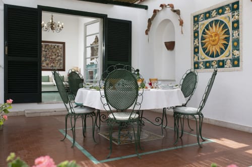 Elegante sala da pranzo della Conciergerie Capri con sedie in ferro battuto verde, tovaglia bianca, opere d'arte con motivi solari e piscina