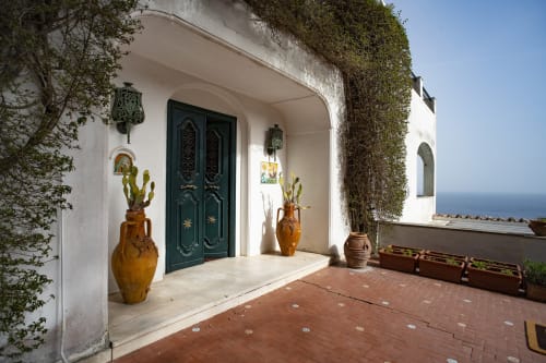Ingresso in stile mediterraneo di La Conciergerie Capri con pareti ricoperte di edera, porte verde scuro e vasi in terracotta